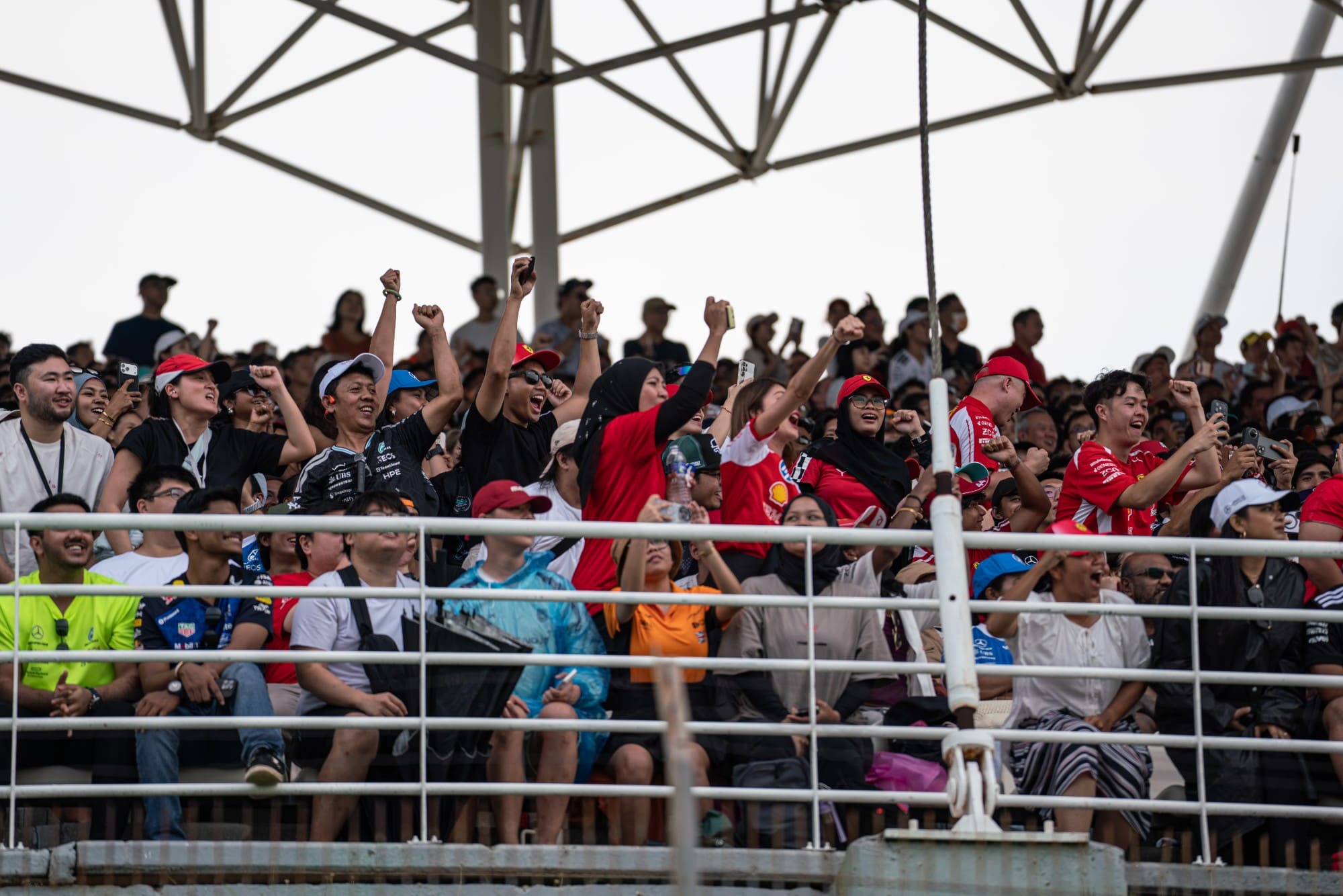 Fans in Ferrari, Mercedes and McLaren colours cheer in the grandstand at Sepang