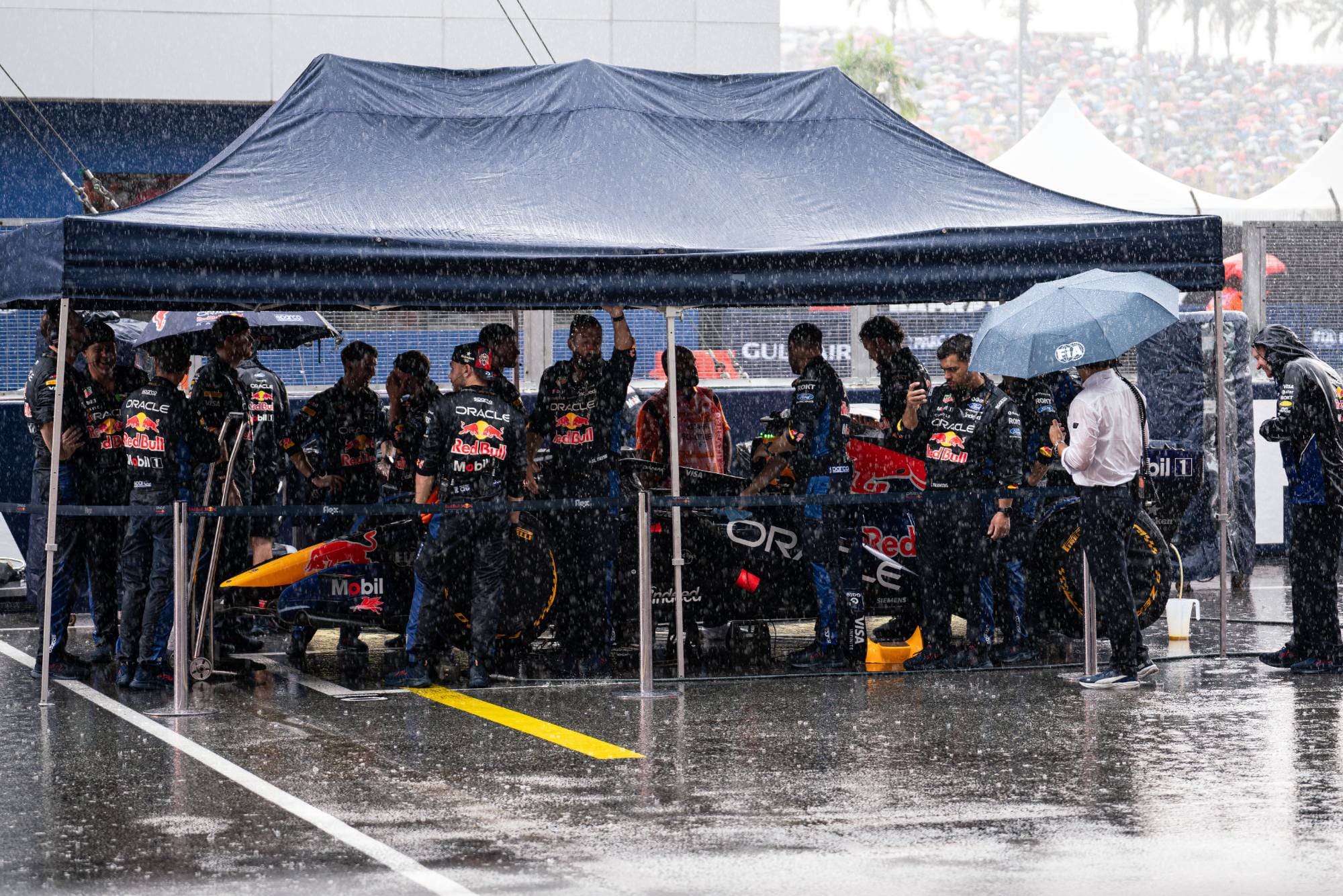 Red Bull mechanics shelter their car under a tent on the grid as heavy rain delays the start at Sepang