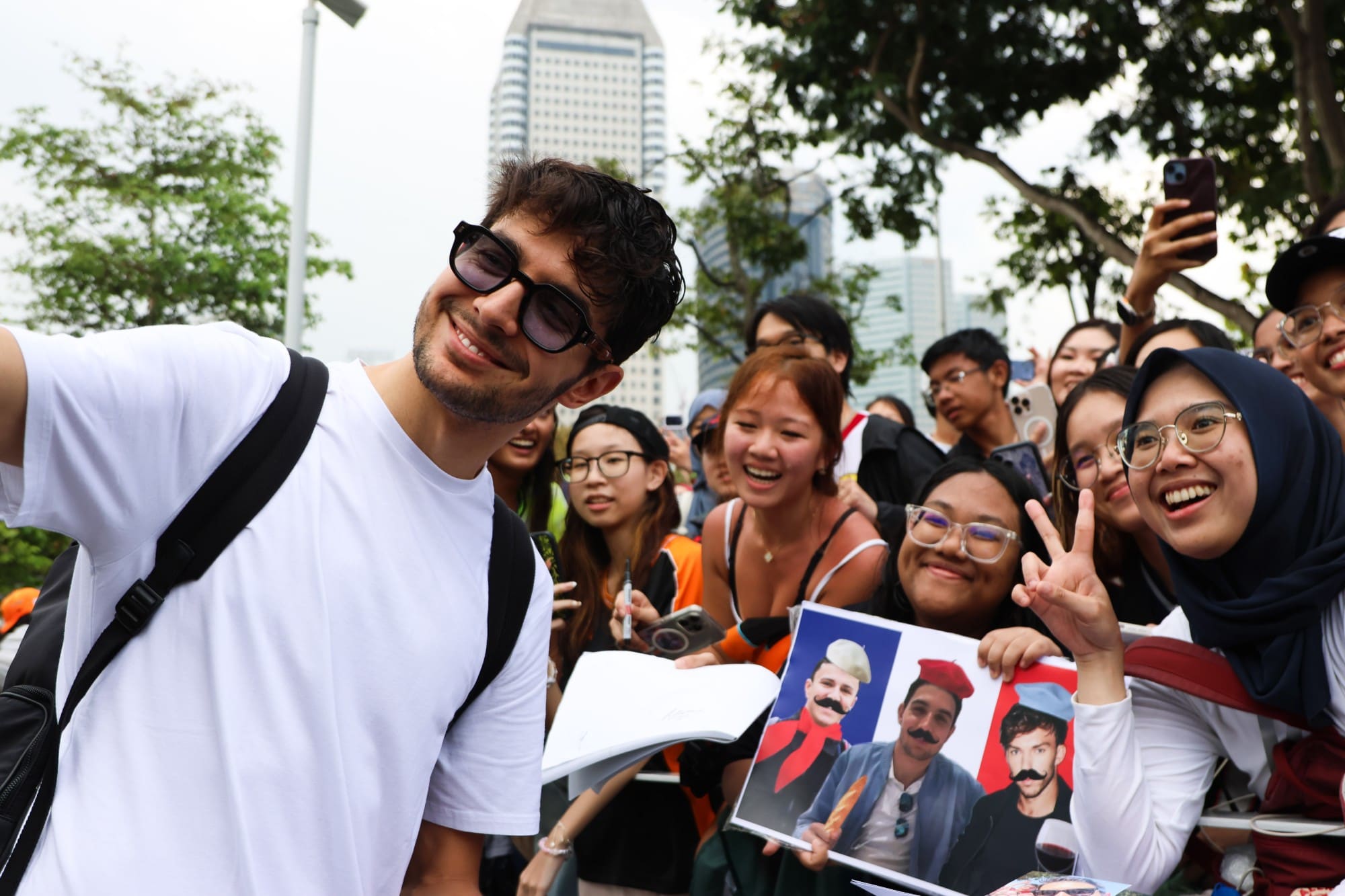 Esteban Ocon takes a selfie with fans holding a homemade sign outside the paddock entrance at the 2025 Singapore Grand Prix