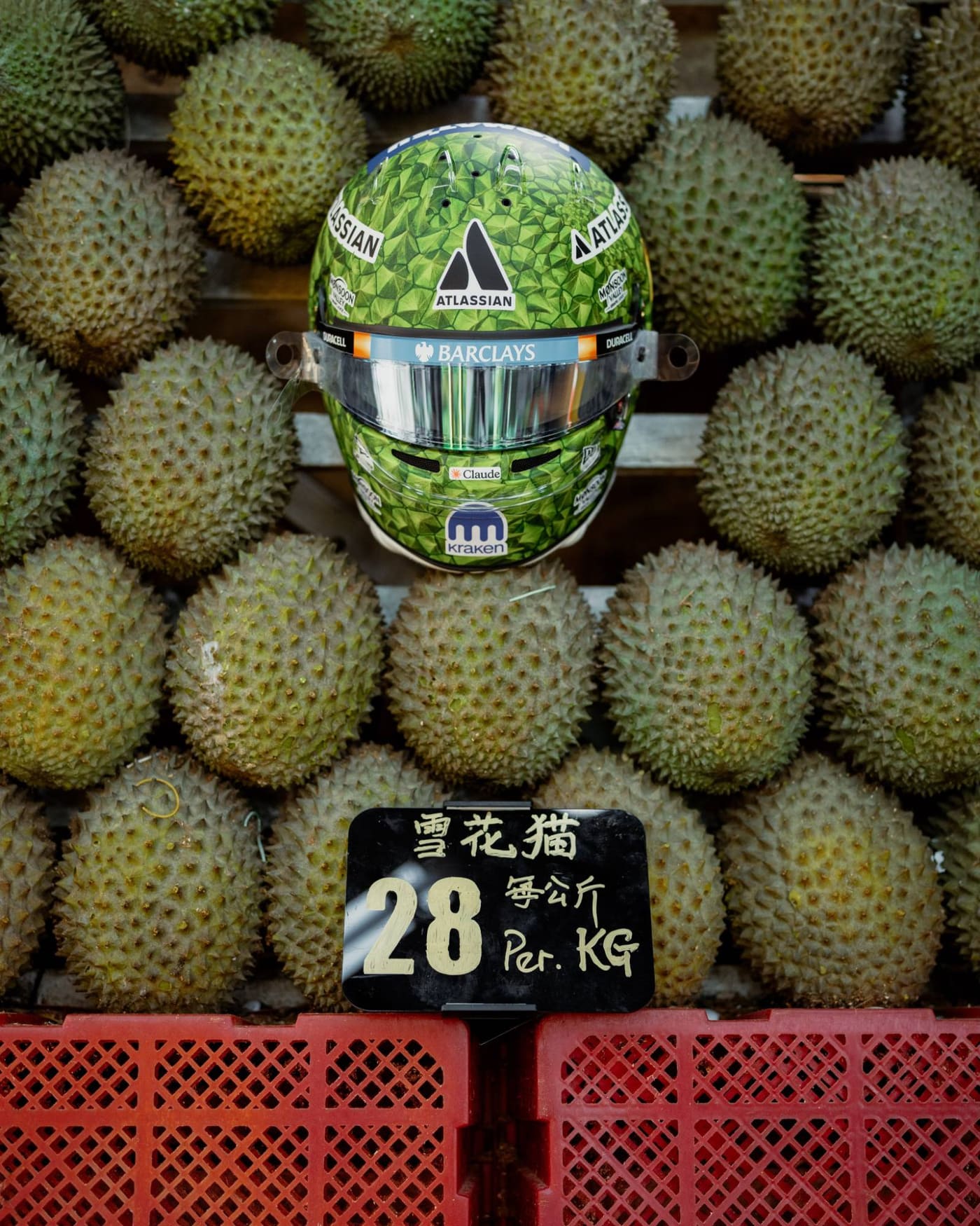 Alex Albon’s durian helmet sits on a pile of durians at a fruit stall, above a handwritten price tag