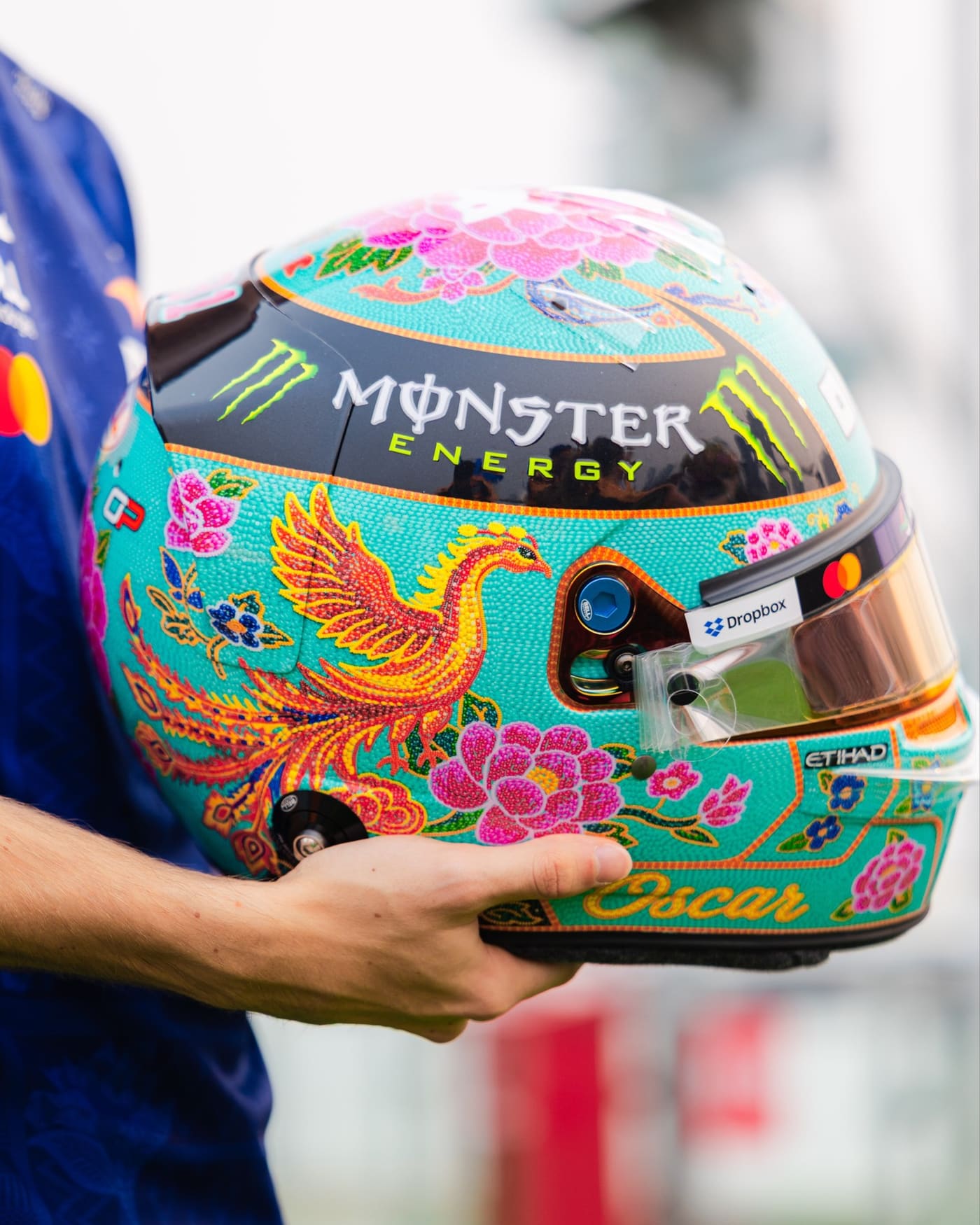 Close-up of Oscar Piastri’s helmet, showing a beaded phoenix and pink peonies on a turquoise base