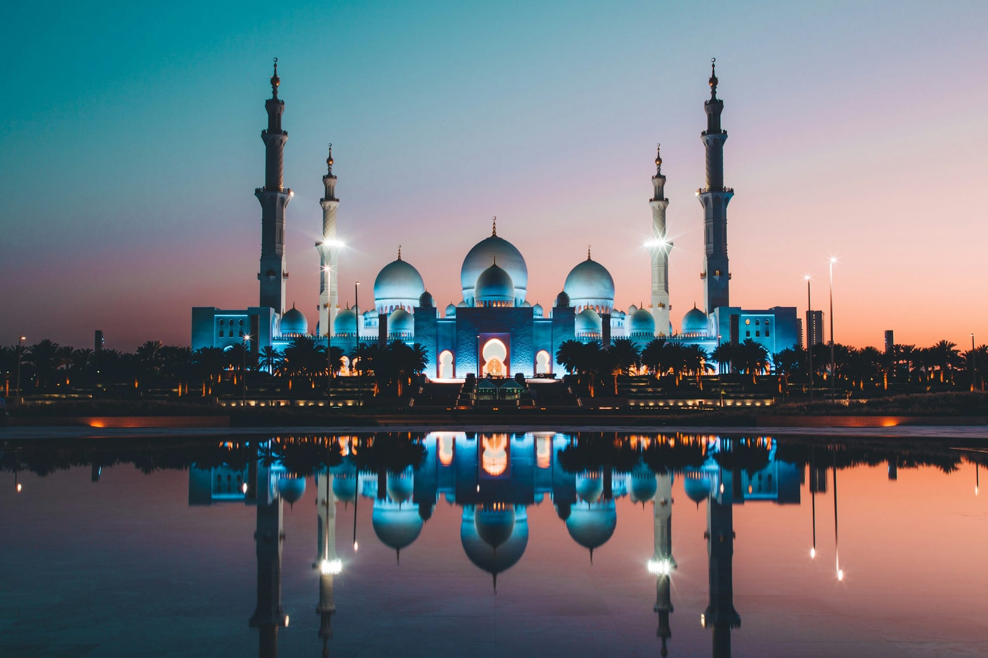 The Sheikh Zayed Grand Mosque lit up at dusk, reflected in a pool