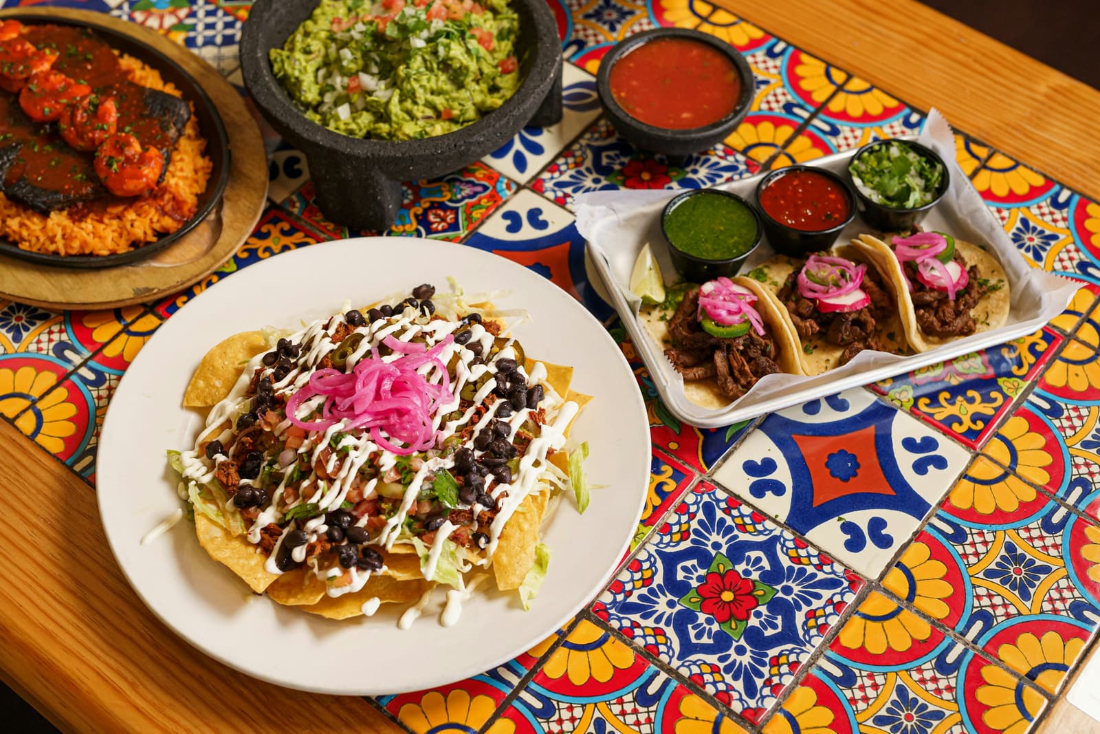 Tacos, tostadas, guacamole and salsas on a tiled table
