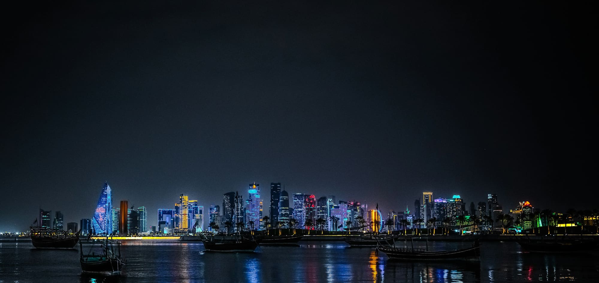 The Doha skyline lit up at night, with dhows on the water