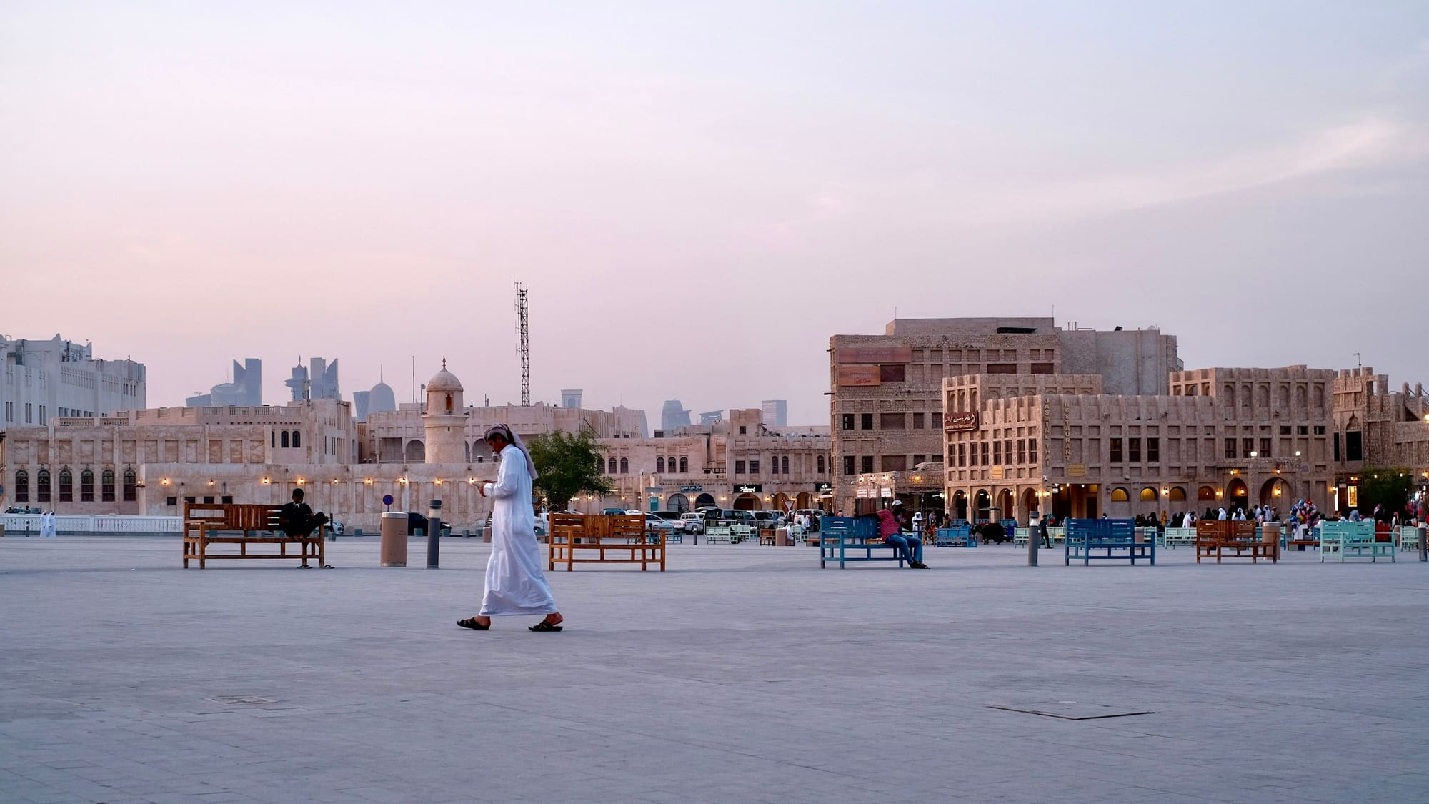A man in a thobe crossing a square in front of Souq Waqif at dusk